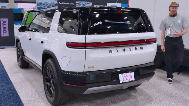 A white Rivian electric vehicle is showcased at an event, with a person pointing at it nearby.
