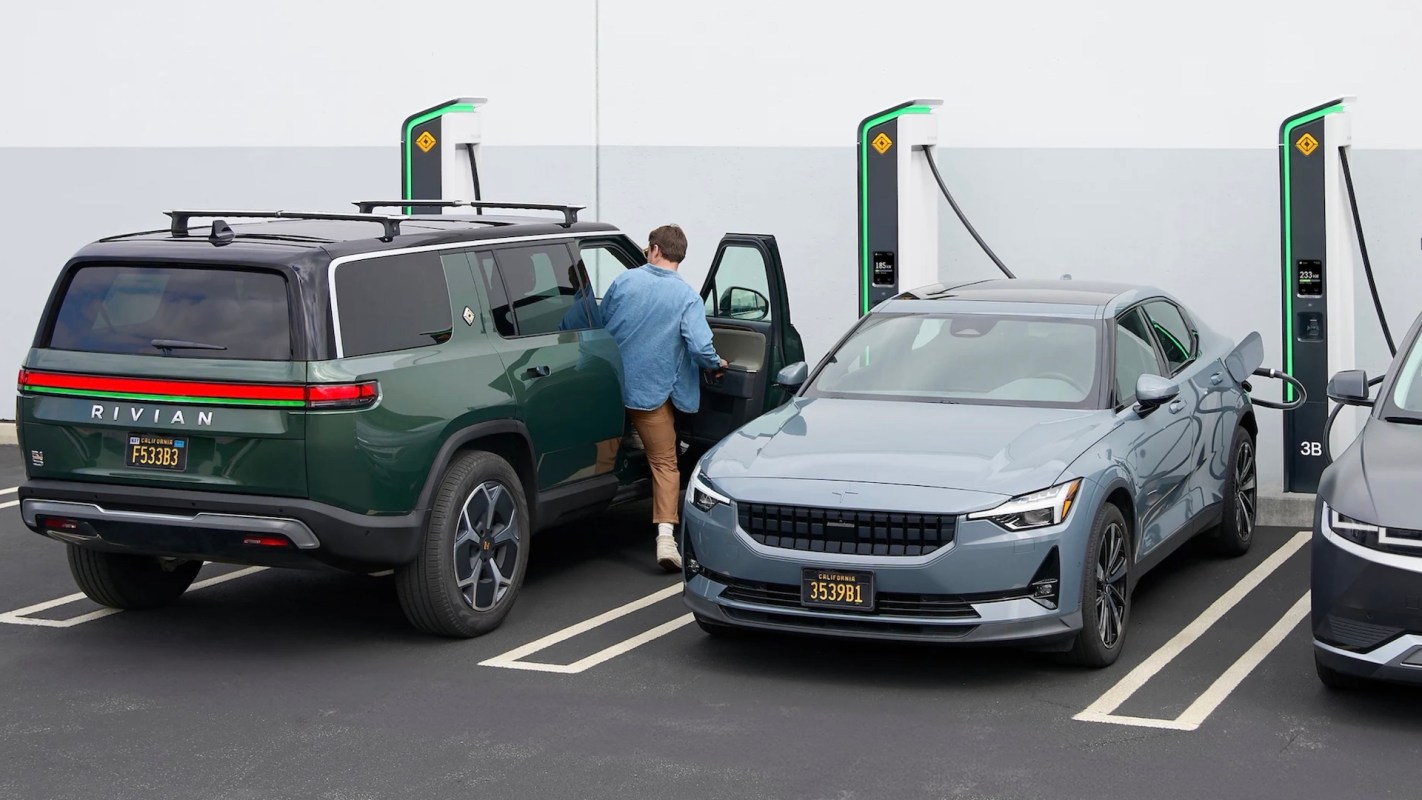 A man entering a green Rivian SUV parked next to a blue Polestar sedan at an electric vehicle charging station.