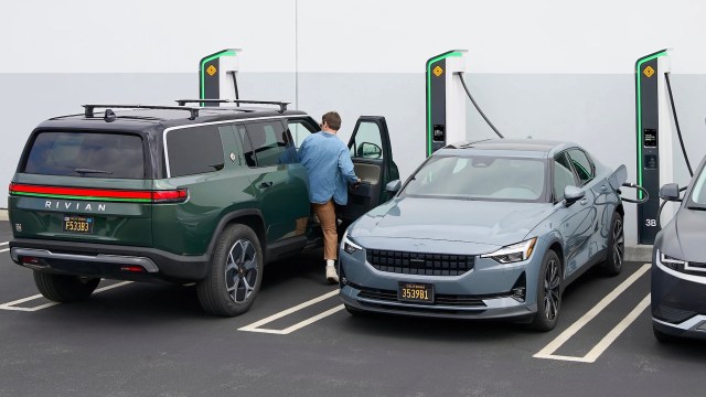A man entering a green Rivian SUV parked next to a blue Polestar sedan at an electric vehicle charging station.