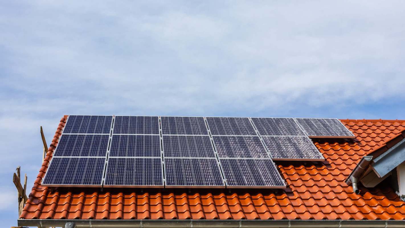 A roof with orange tiles featuring several solar panels against a blue sky.