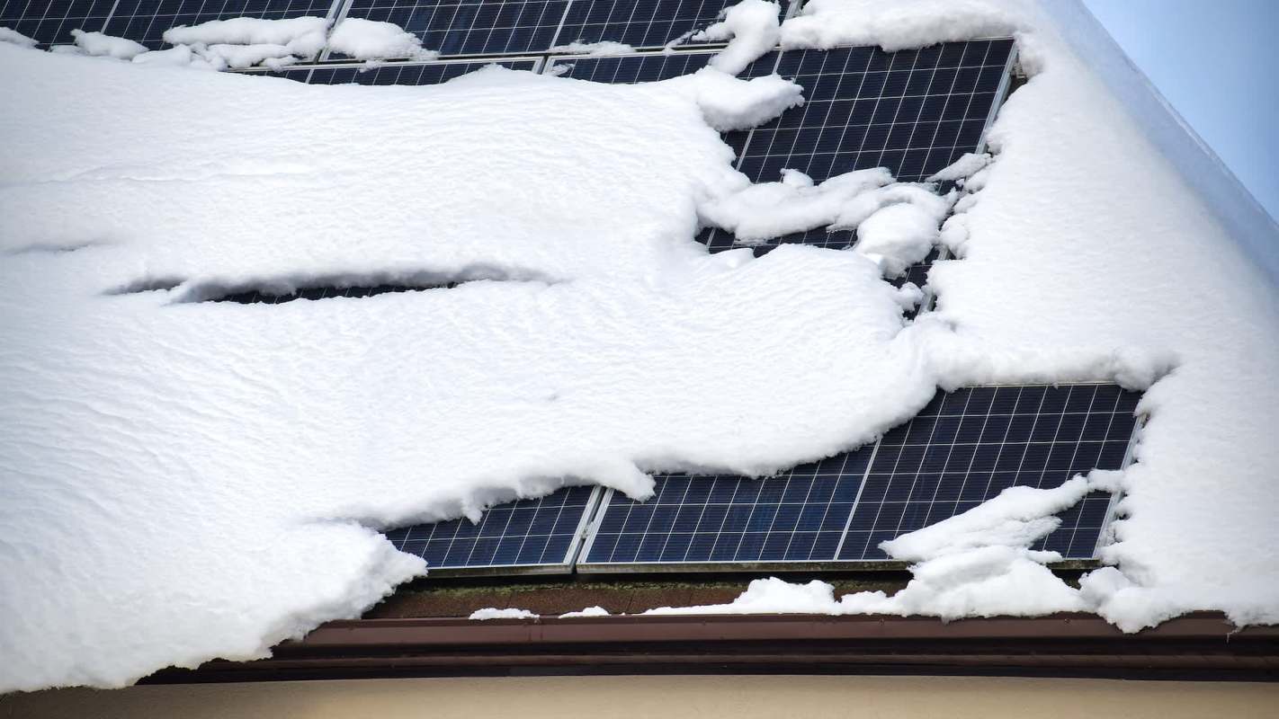 A roof covered in snow partially conceals solar panels beneath.
