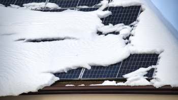 A roof covered in snow partially conceals solar panels beneath.