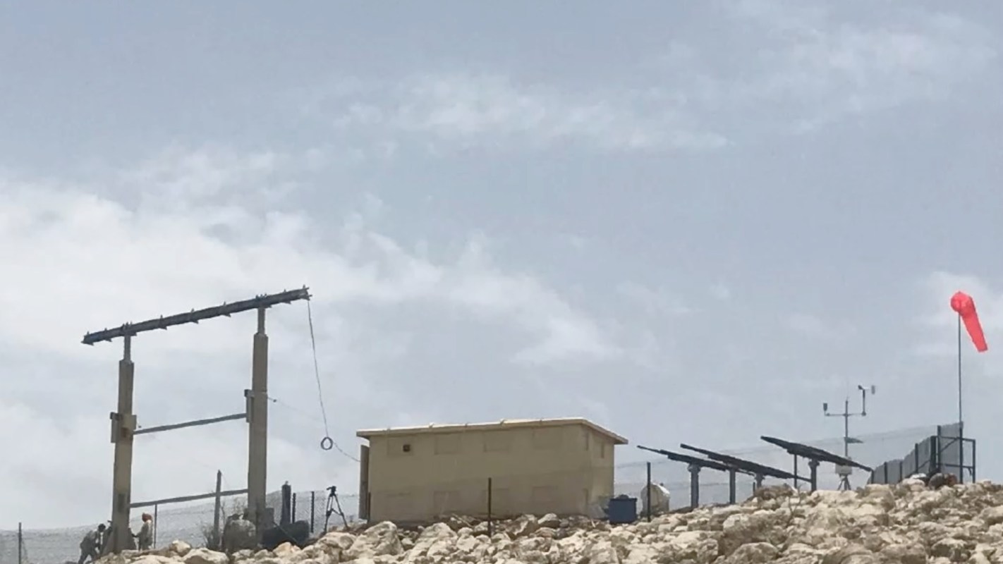 A small structure with a flag and equipment on rocky terrain under a cloudy sky.