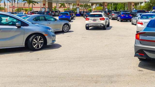 A busy gas station with several cars waiting in line under sunny weather.