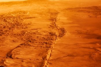 A desolate, reddish landscape featuring rugged terrain and distant mountains under an orange sky.