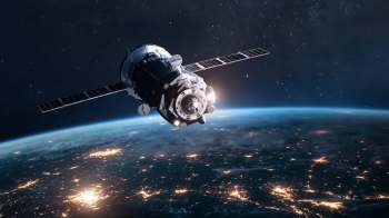 A satellite orbits Earth, illuminated against a backdrop of stars and city lights below.