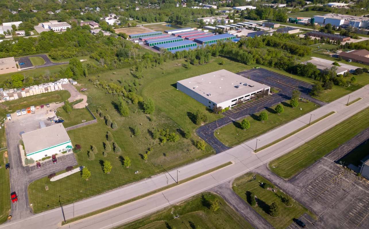 An aerial view of a commercial area with green fields, parking lots, and storage units in the background.