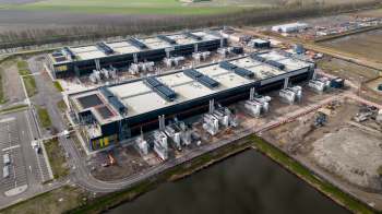 An aerial view of an industrial complex with multiple buildings and equipment under construction near a body of water.