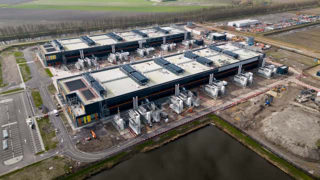 An aerial view of an industrial complex with multiple buildings and equipment under construction near a body of water.