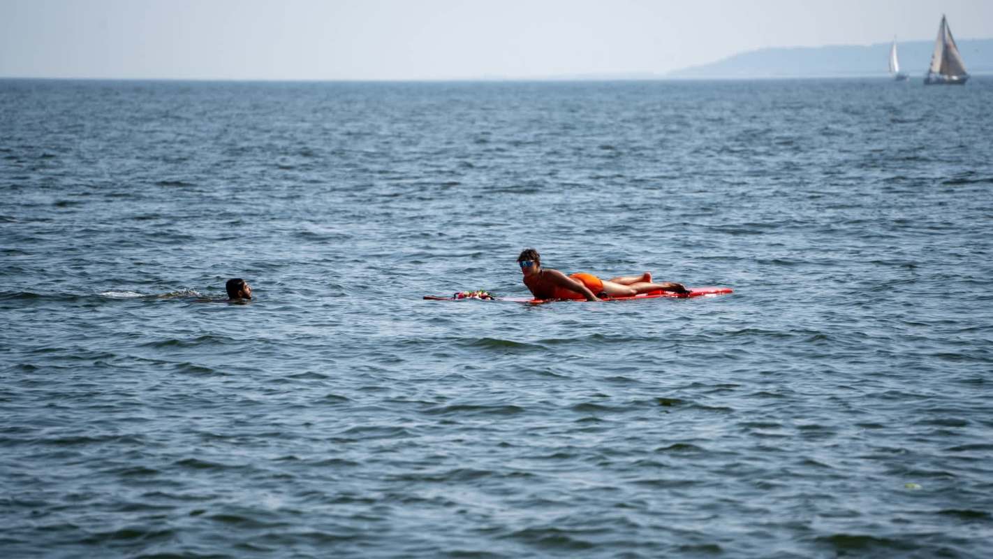 A person swims in the water waiting for a lifeguard approaching on a paddleboard.