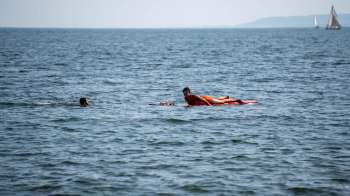 A person swims in the water waiting for a lifeguard approaching on a paddleboard.