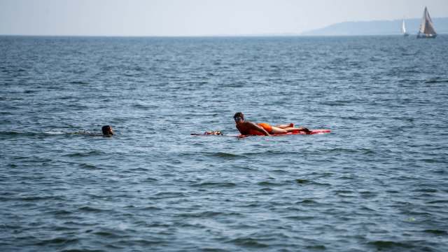 A person swims in the water waiting for a lifeguard approaching on a paddleboard.