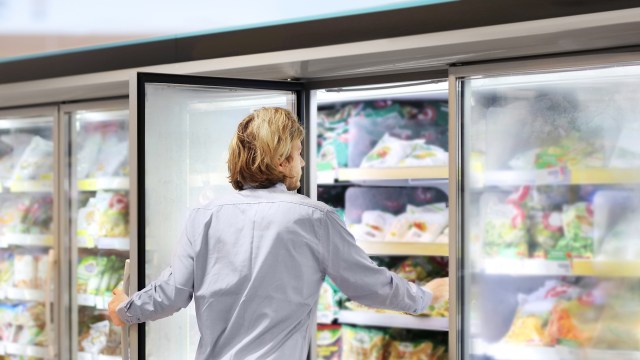 A person reaching into a freezer at a grocery store.