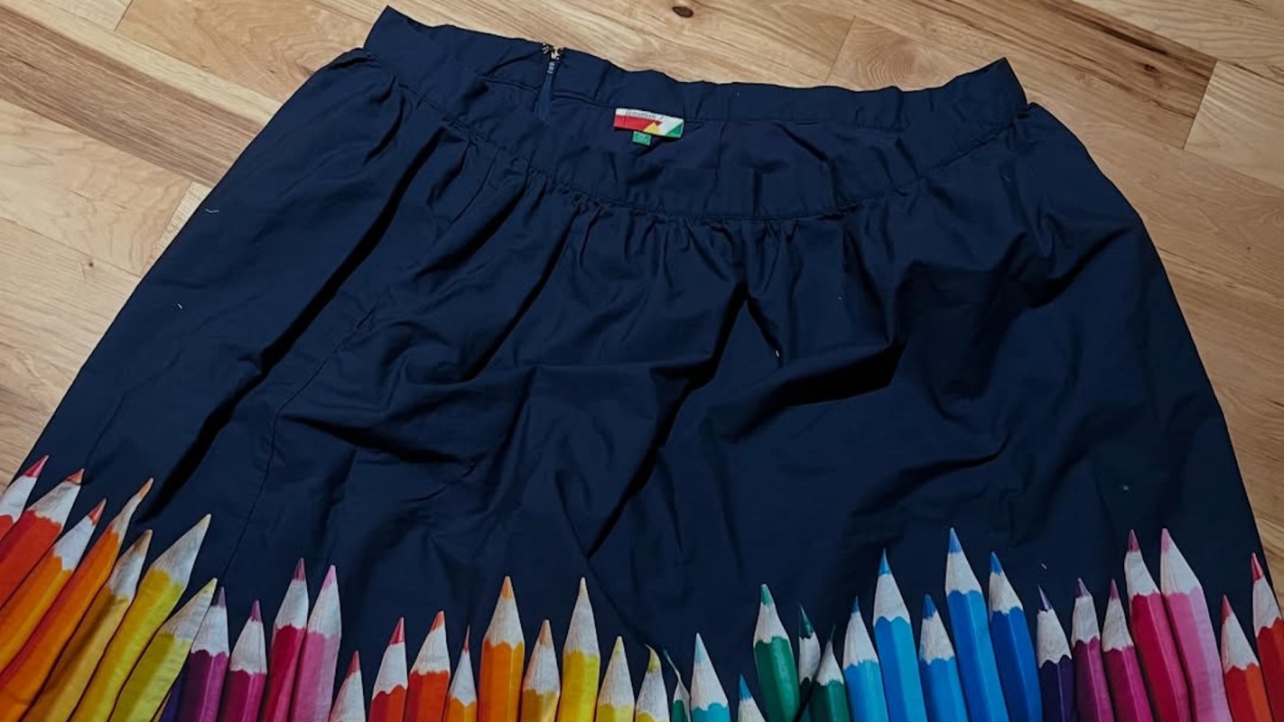 A navy skirt featuring a colorful pencil design along the hem, placed on a wooden floor.