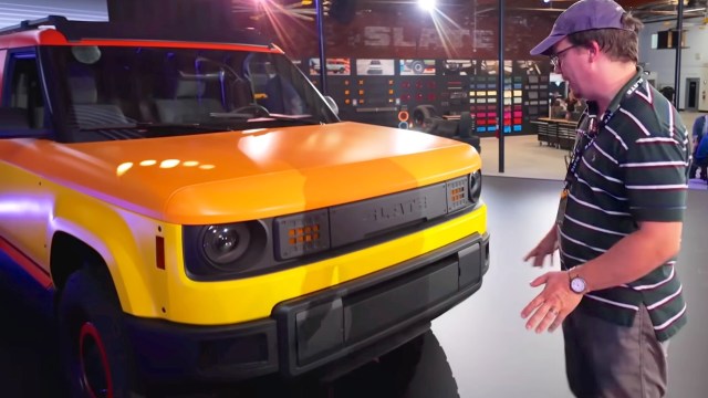 A man examines a yellow and orange electric vehicle.