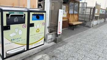 Two bins for waste disposal beside a wooden bench at a bus stop.