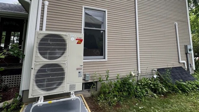 An outdoor air conditioning unit is installed next to a home's beige siding, with a window visible above it.
