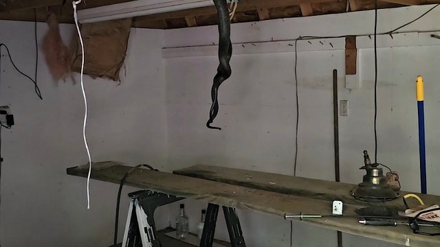 A cluttered workshop with a wooden table, tools, and a snake hanging from the ceiling.