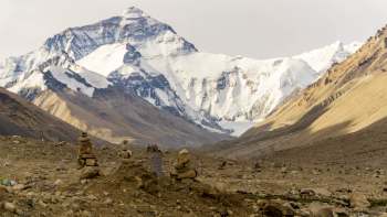 A rocky landscape with stacked stones in the foreground and Mount Everest in the background.