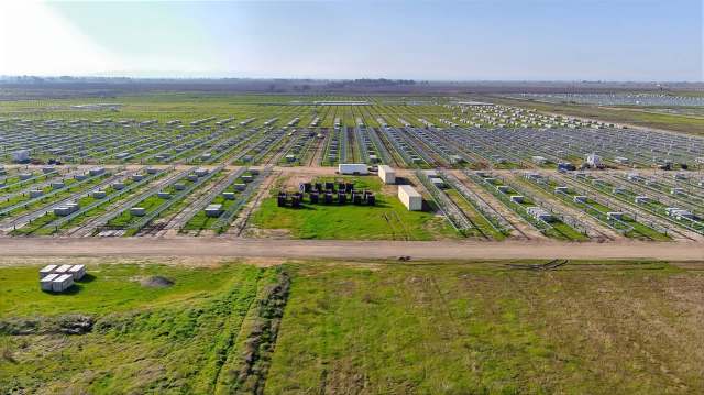 Aerial view of a large agricultural field with rows of green plants and battery storage containers.
