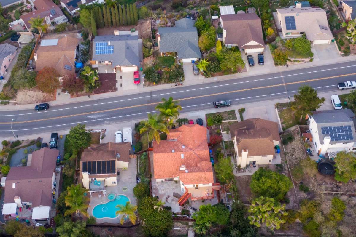 An aerial view of suburban homes with gardens, a pool, and a road running through the neighborhood.