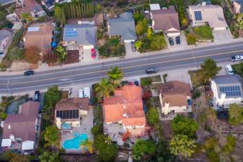 An aerial view of suburban homes with gardens, a pool, and a road running through the neighborhood.