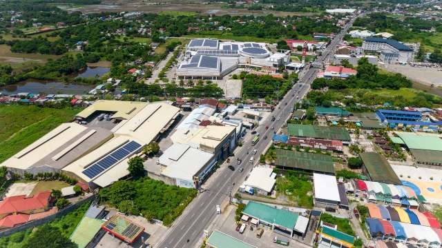 An aerial view of a mixed urban landscape featuring commercial buildings, houses, and greenery along a busy road.
