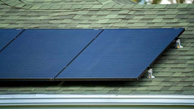 A close-up of solar panels installed on a green shingled roof.