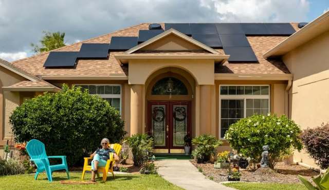 A woman relaxes in a yellow chair outside her home, which features solar panels on the roof.