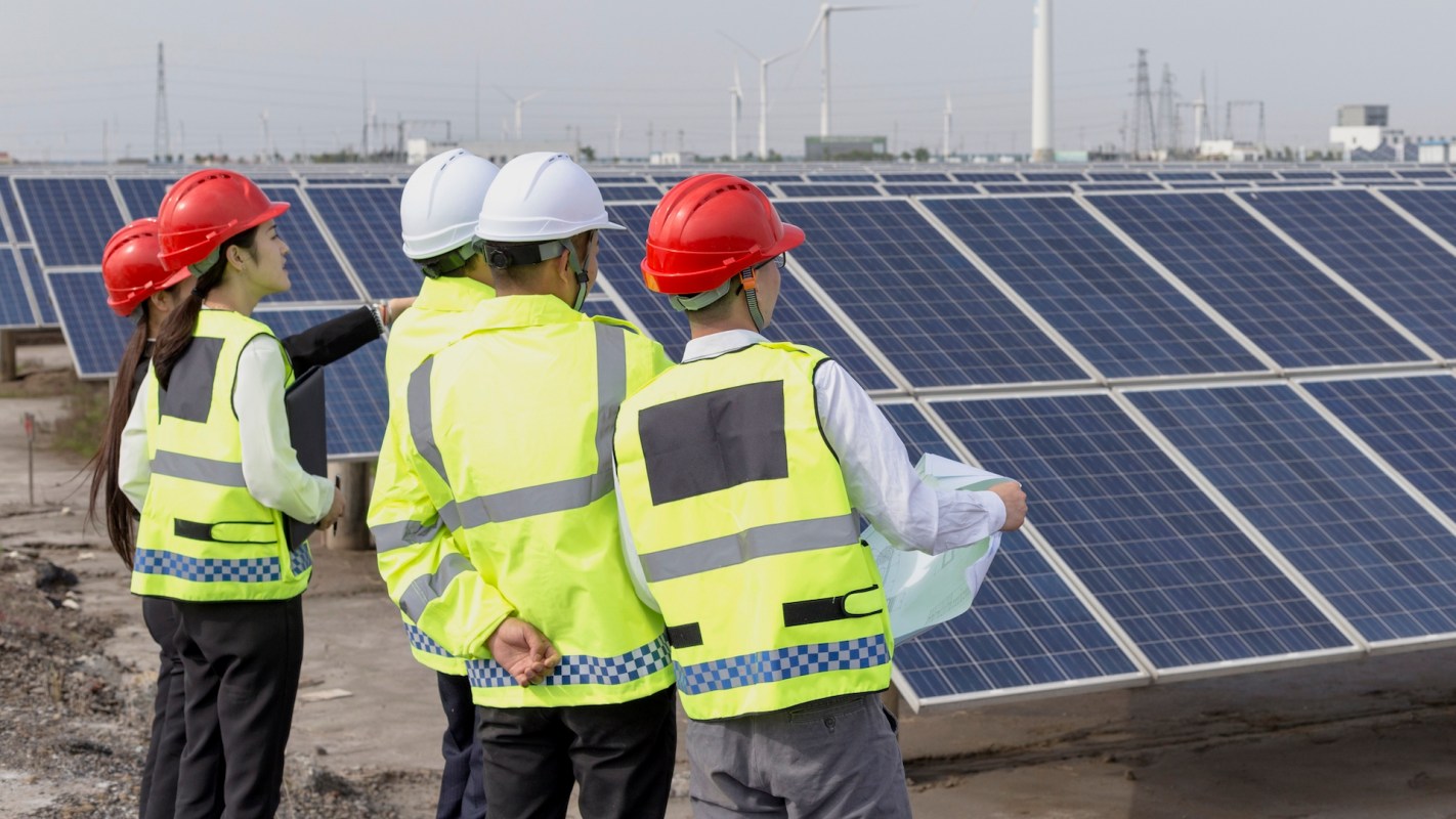 A group of workers in safety gear inspecting solar panels at a renewable energy site.