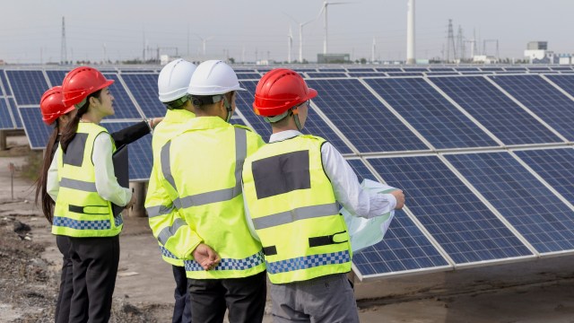 A group of workers in safety gear inspecting solar panels at a renewable energy site.