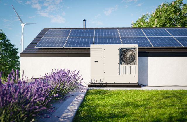 A house with solar panels, a heat pump, and lavender plants in the garden.