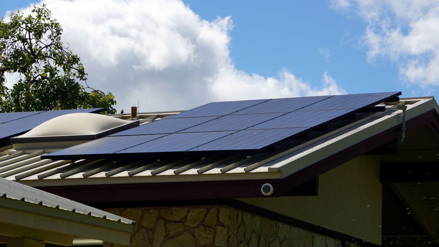 Solar panels on the roof of a house under a partly cloudy sky.