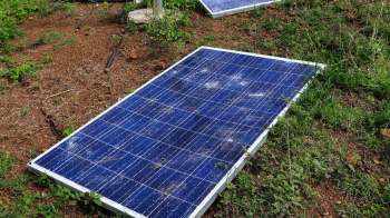 Three solar panels lying on the ground amid grass and dirt.