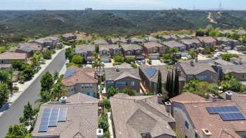 An aerial view of a suburban neighborhood, including houses with solar panels.