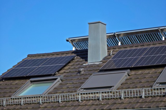 Solar panels on a sloped roof with a chimney against a clear blue sky.