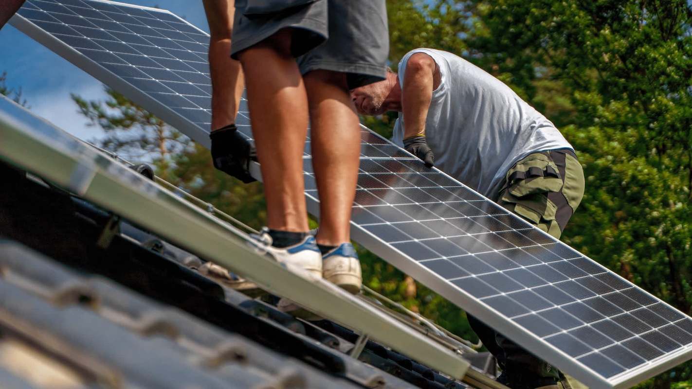 Two workers install solar panels on a rooftop.
