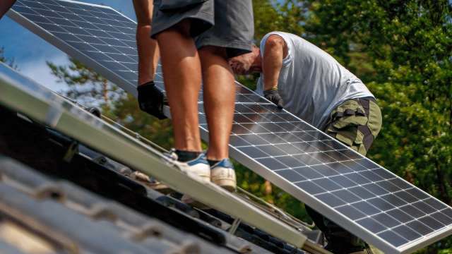 Two workers install solar panels on a rooftop.