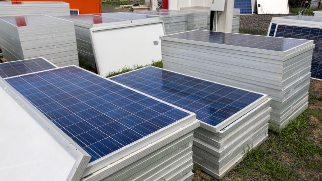 Stacks of solar panels resting on metal frames in a grassy area.