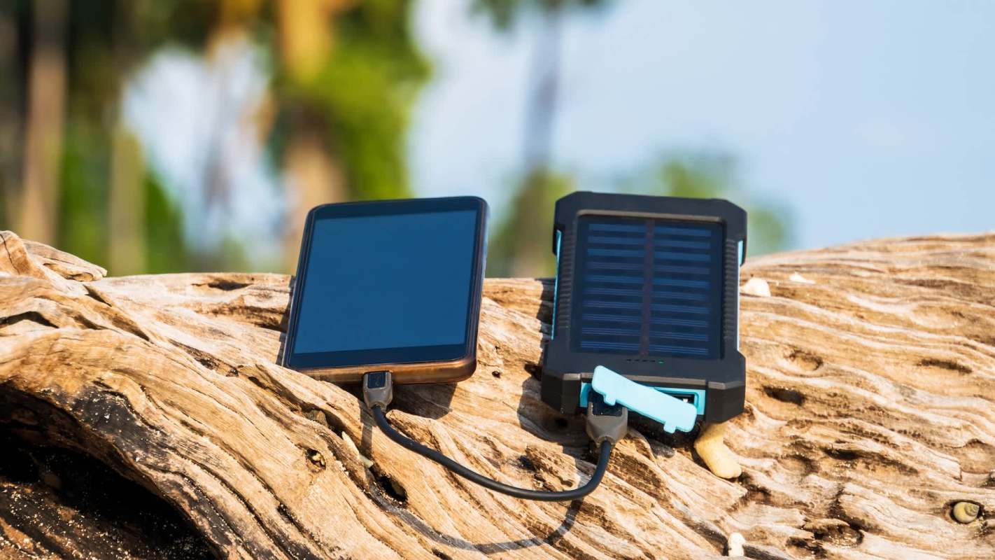 A solar power bank charging a phone on a natural wooden surface.