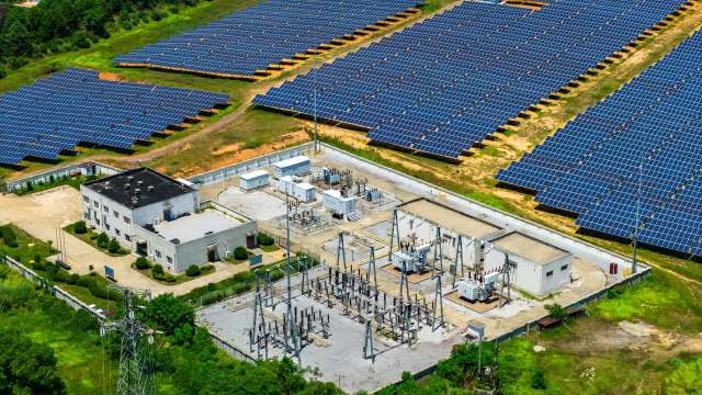 An aerial view of a solar farm with numerous solar panels and an adjacent electrical facility.