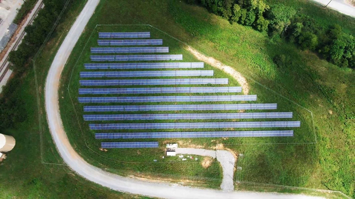 An aerial view of a solar panel array arranged in rows on a grassy field.