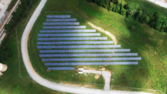 An aerial view of a solar panel array arranged in rows on a grassy field.