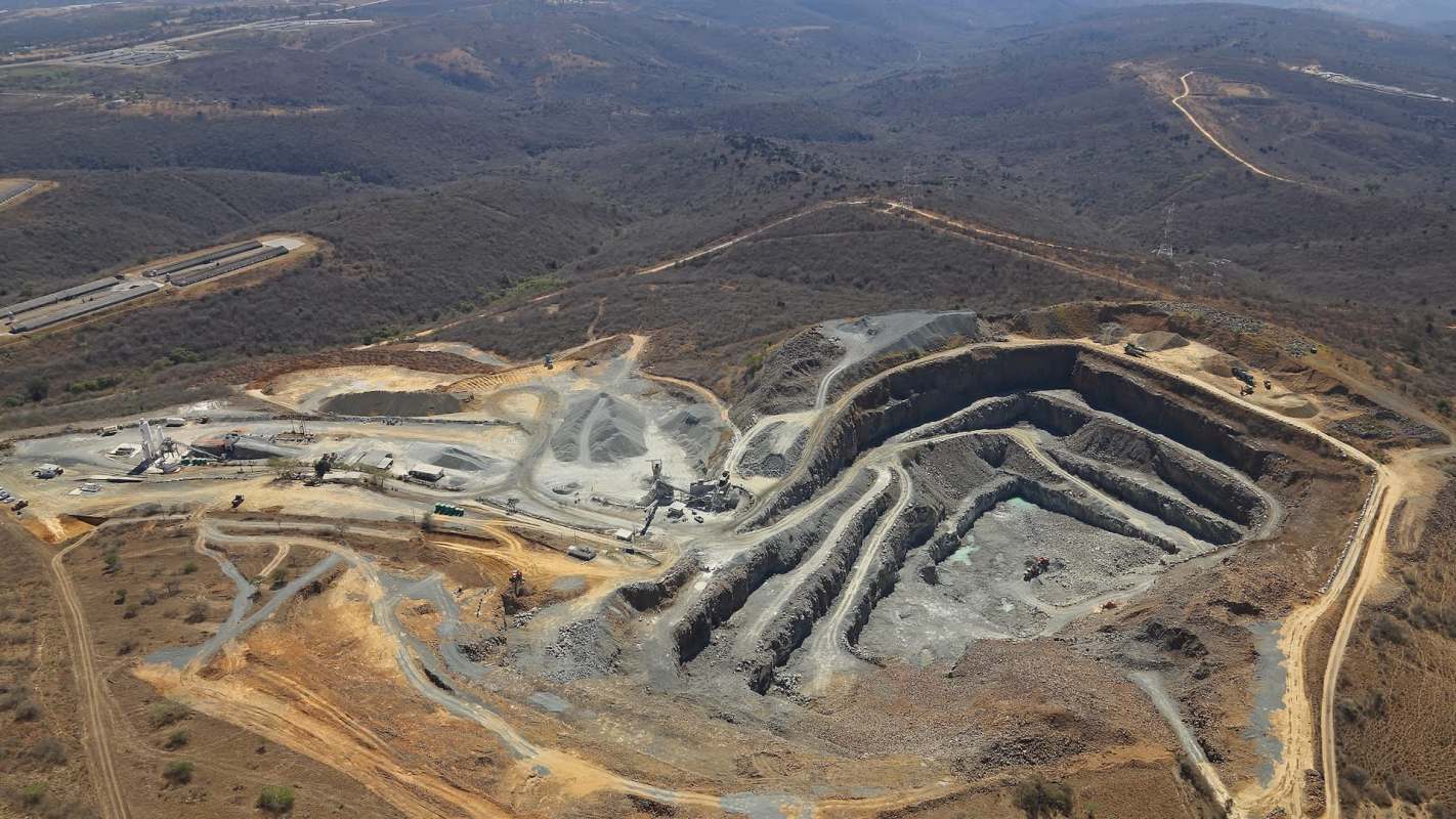 An aerial view of a mining site showing excavated earth, machinery, and surrounding hilly terrain.