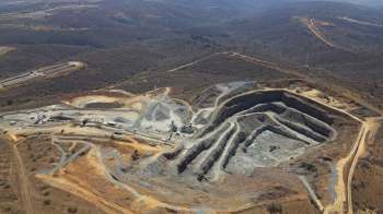 An aerial view of a mining site showing excavated earth, machinery, and surrounding hilly terrain.