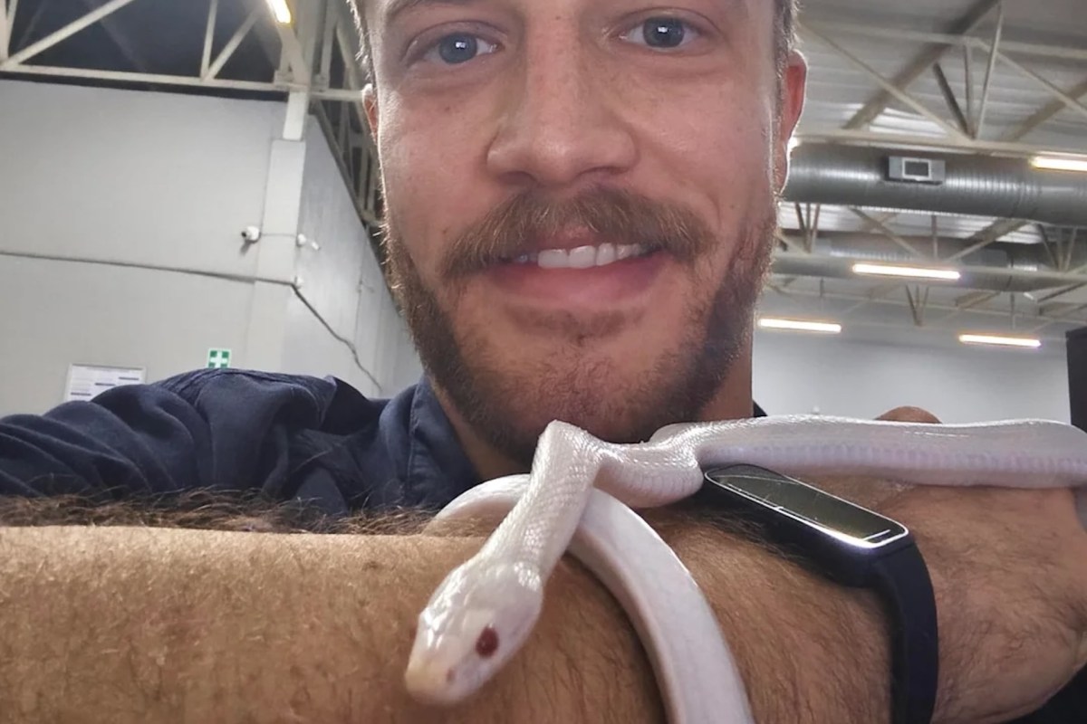 A man smiles while holding a white snake on his arm in a well-lit indoor setting.