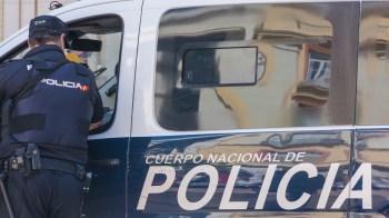 A police officer interacting with a police van marked "Cuerpo Nacional de Policía."
