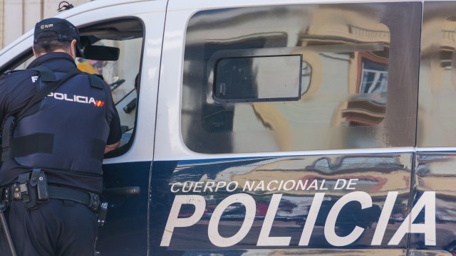 A police officer interacting with a police van marked "Cuerpo Nacional de Policía."