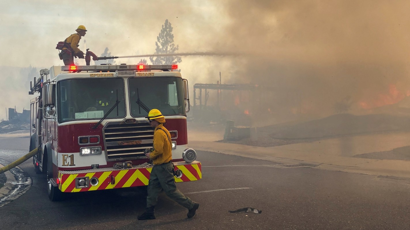A firefighter sprays a fire while standing on a firetruck.
