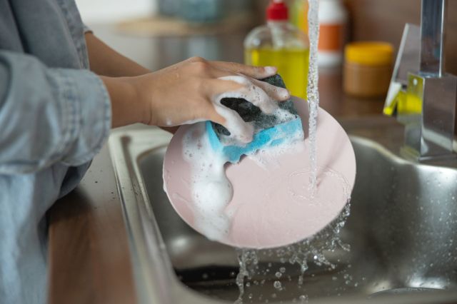 A person washes a dish with a kitchen sponge.